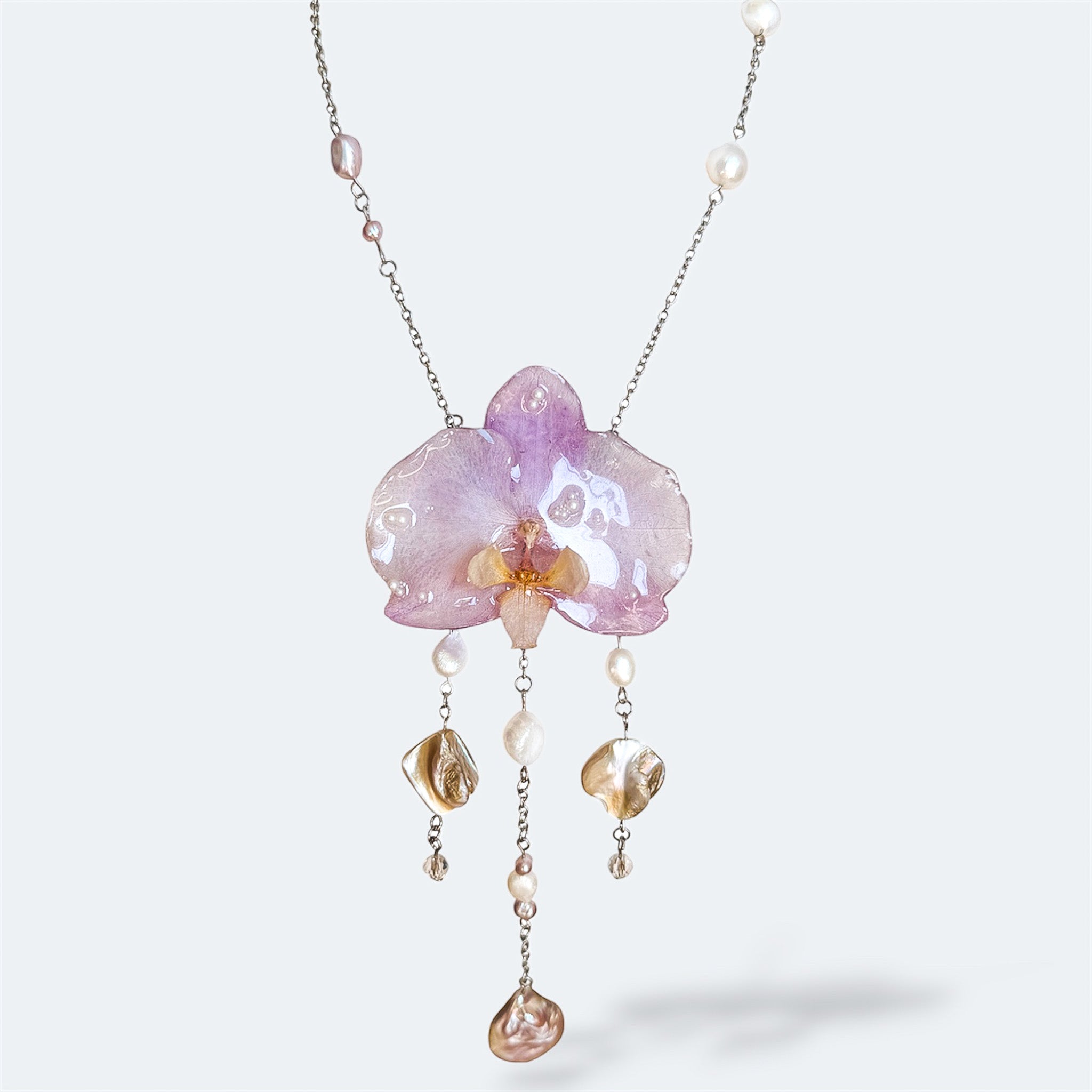 Collar con orquídea lila encapsulada en resina, sobre cadena de acero inoxidable con perlas de agua dulce