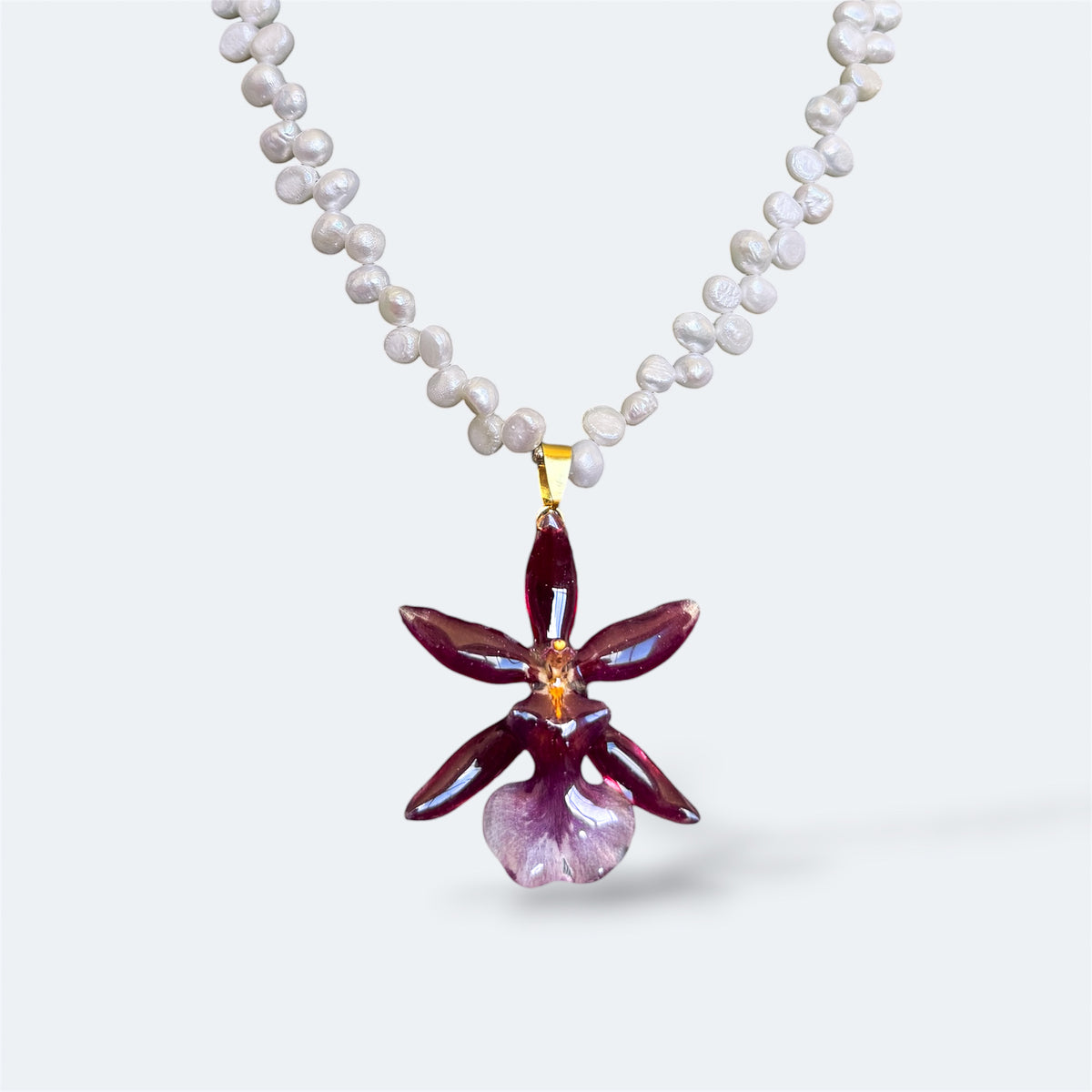 Collar con orquídea Cambria burdeos encapsulada en resina, sobre cadena de perlas naturales de agua dulce