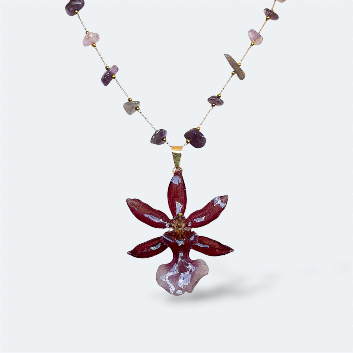 Collar con orquídea Cambria burdeos encapsulada en resina, sobre cadena de amatistas y acero inoxidable
