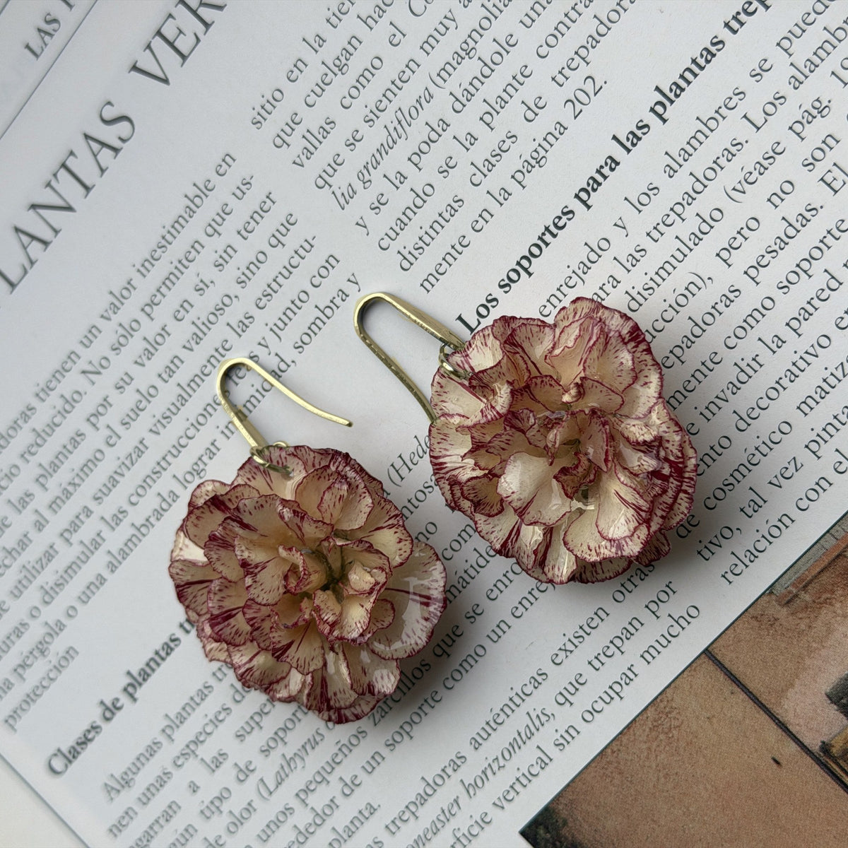 Pendientes Clavel Nácar con anzuelo dorado y un clavel, sobre un libro de plantas